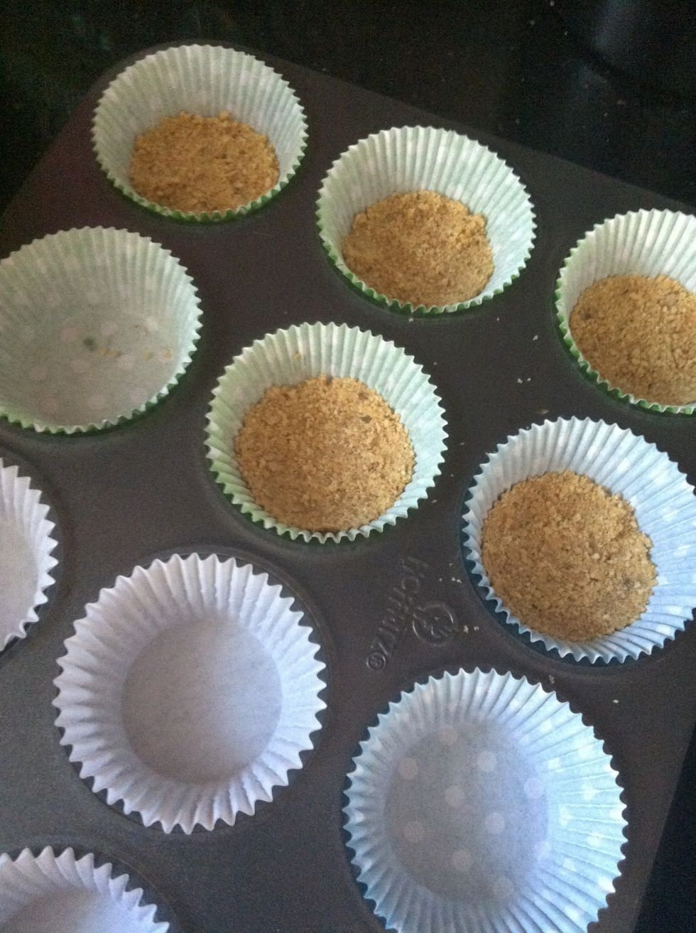 Spoon evenly amongst your lined cupcake tins. Use a cup to compress your graham crackers to form the crust.