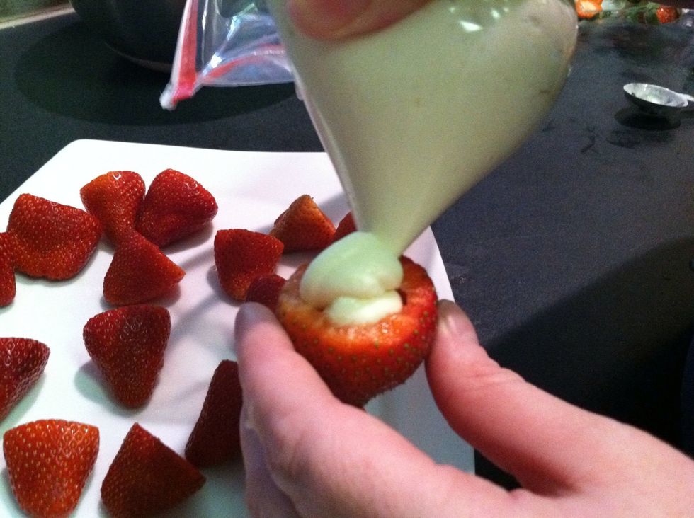 Spoon the cheesecake filling into a pastry pipe. (These are pretty cheap in baking aisle at grocery stores.) Then squeeze the filling into the strawberries swirling upward as you go.