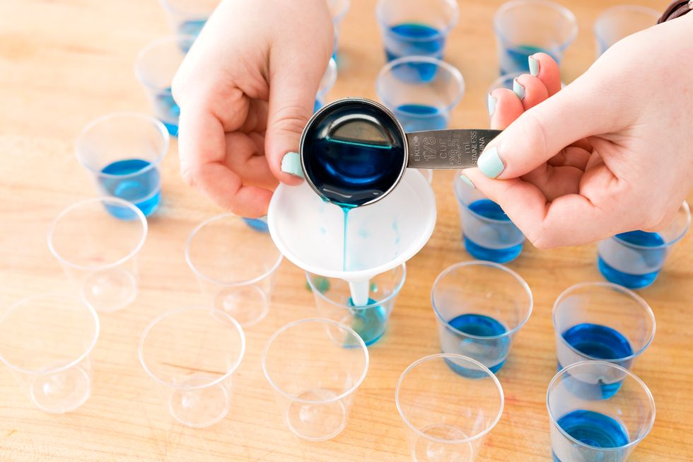 Spoon your blue JELL-O into small plastic shot glasses. We used a small funnel to reduce splashing. Refrigerate for about 15 minutes until blue layer is set.