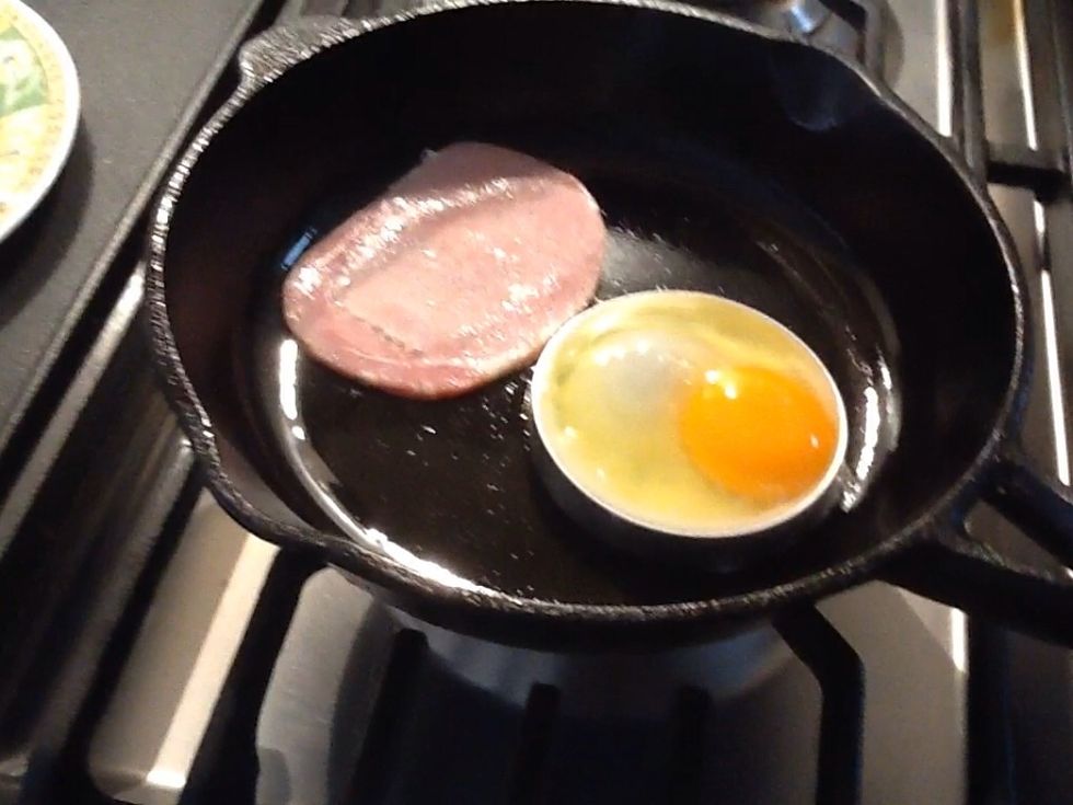 Spray a frying pan with canola spray oil. Crack the egg and put the contents into the ring, and place one piece of bacon in the pan as well