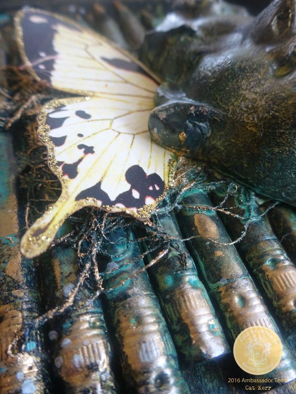 Spray the piece with any color shine spray. I used Color Bloom 2 Dragonfly Blue. Any shimmery spray will work.then I added glitter to the edges of a butterfly wing and then glued it in place