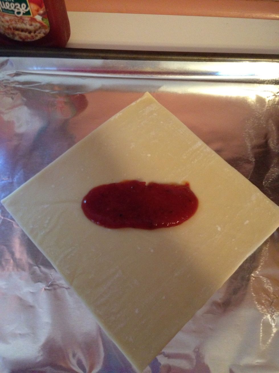 Spread 1 TBS of pizza sauce horizontally across center of wrapper.
