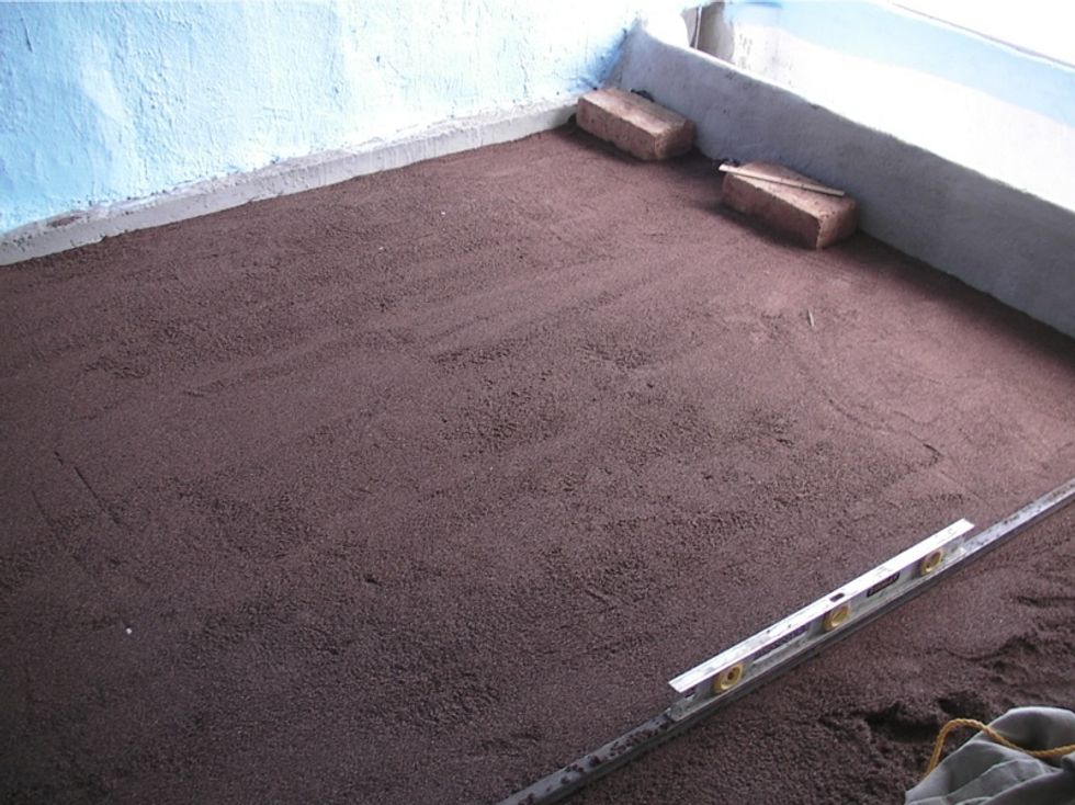 Spread a layer of finely screened sand over the floor area. Make sure it is compacted and level. From here on, you will need to stand on boards to avoid putting foot prints in your floor base.