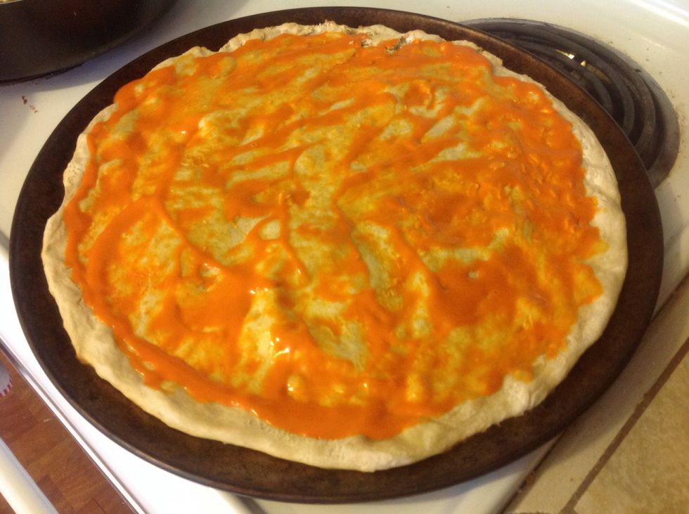 Spread a thin layer of wing sauce across the prepared crust.