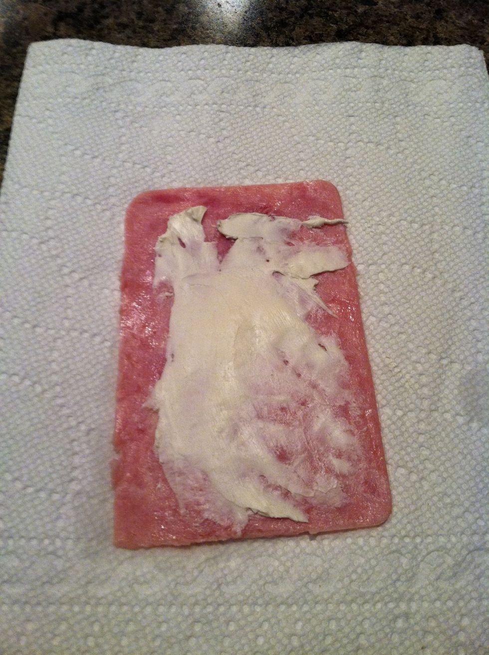 Spread cream cheese onto a piece of ham.