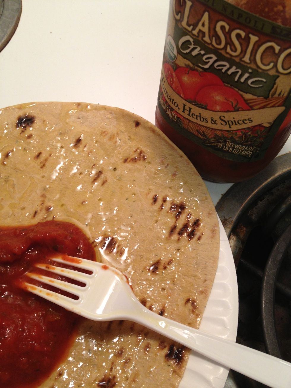 Spread sauce onto the flatbread. My wife likes to rub a garlic clove over the flatbread, instead of sauce. Spread within about a half inch from the edge of the flatbread so you have a little crust.