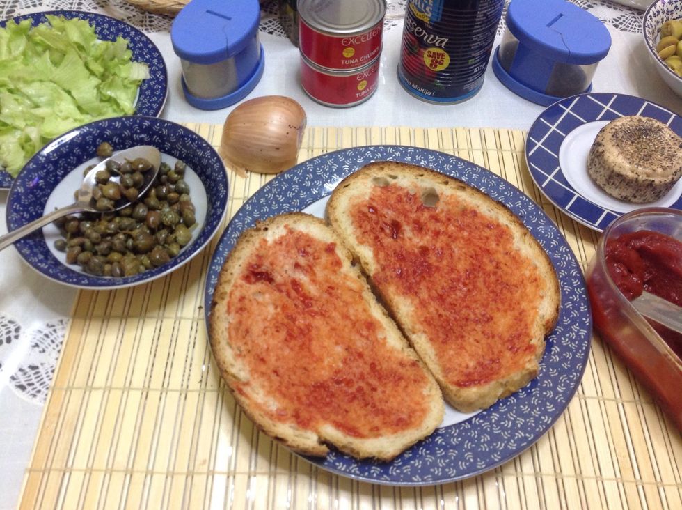 Spread tomato paste over slices of Maltese bread.