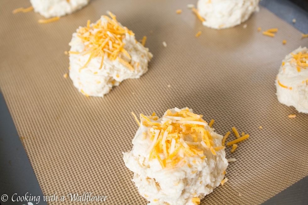 Sprinkle extra cheddar cheese over each biscuit before placing the baking sheet into the oven to bake for about 12-14 minutes or until the top of the biscuits are golden brown.