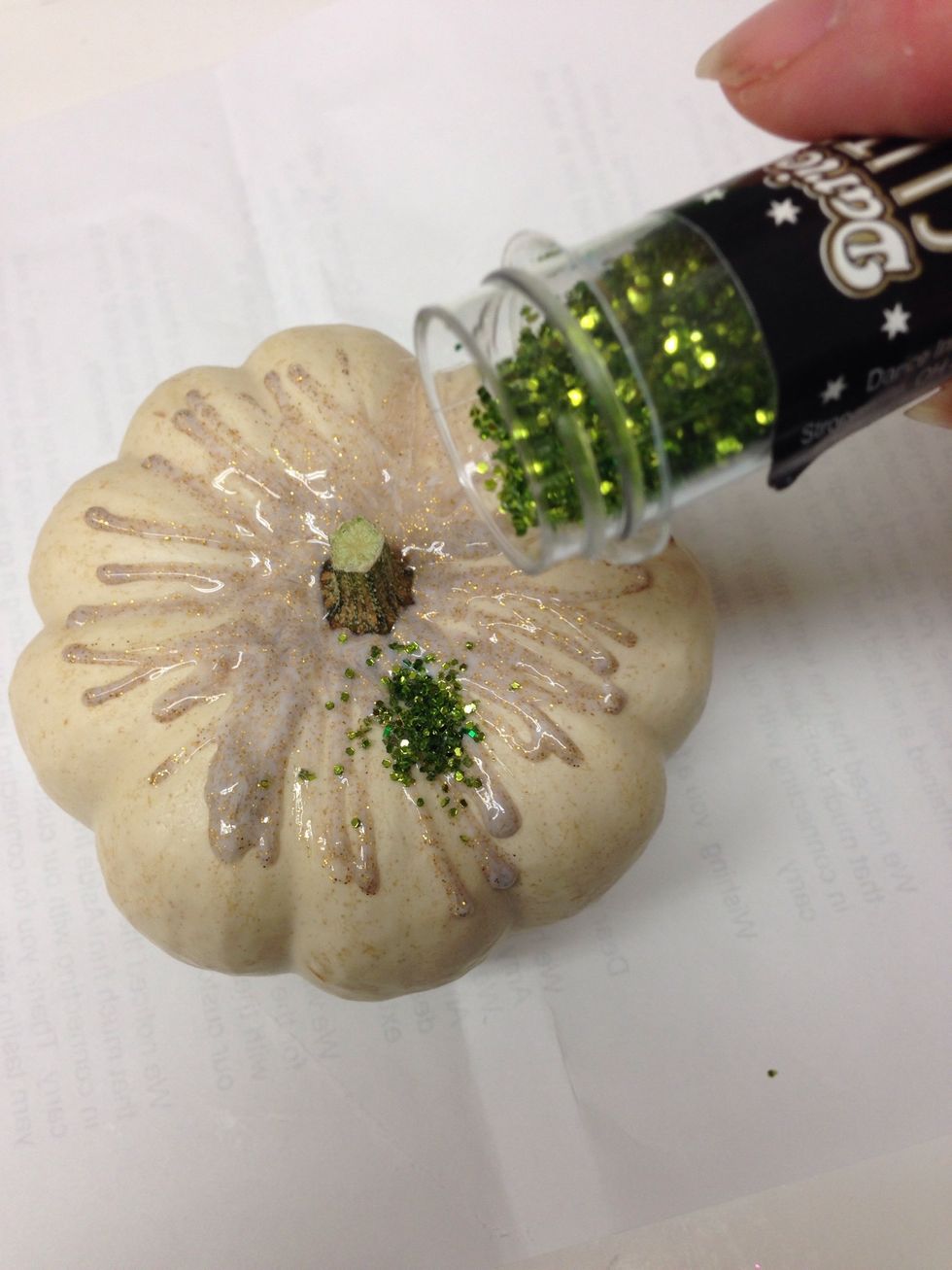 Sprinkle glitter around the top of your pumpkin. You can use more than one color if you like. it's helpful to have a piece of scrap paper under your pumpkin to catch the extra glitter.