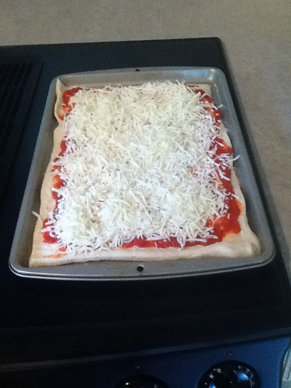 Sprinkle mozzarella cheese on top of the pizza until it is spread evenly across the edges of the dough.