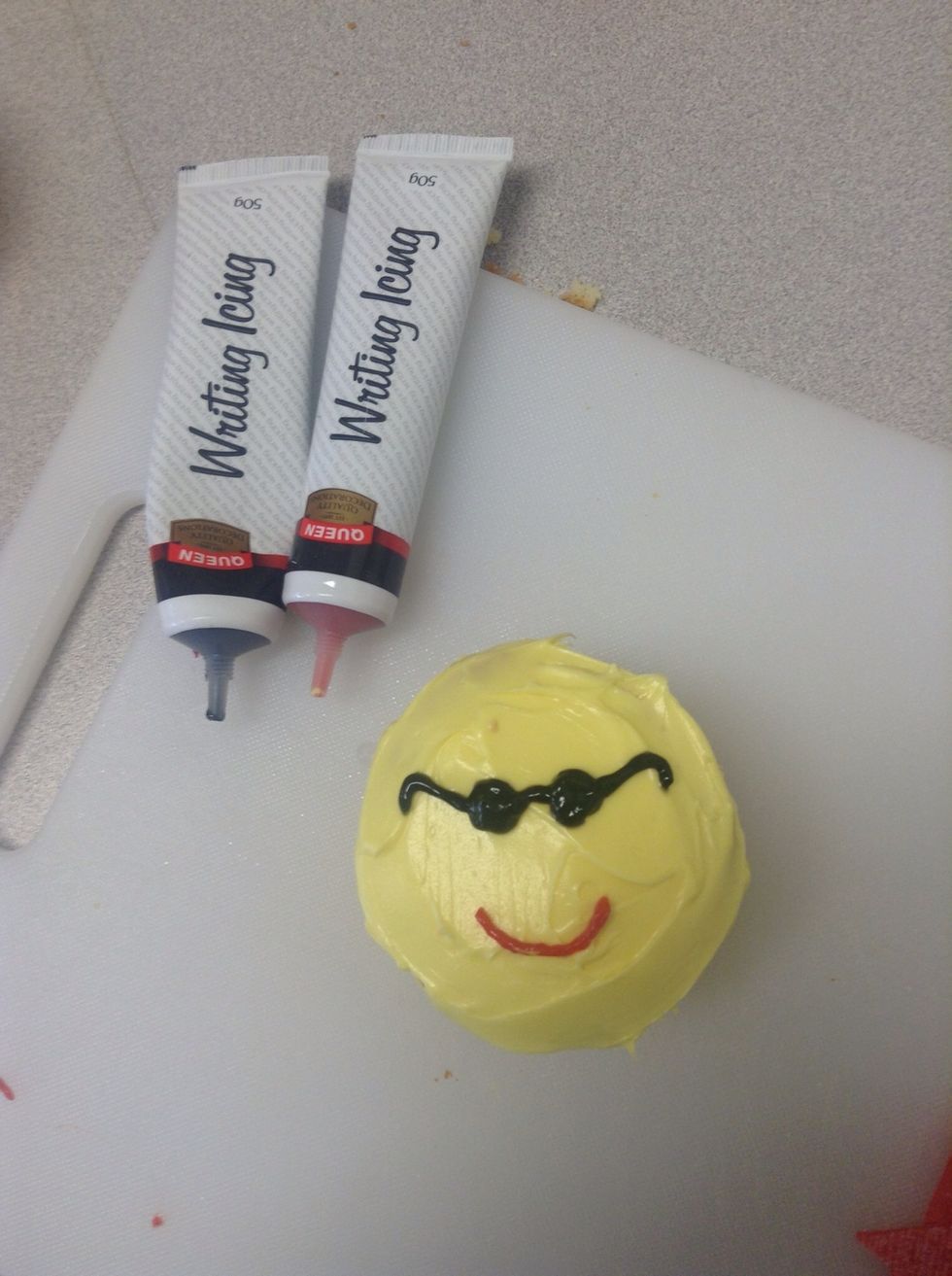 Squeeze the black gel writing icing to make sunglasses for Mr. Sun and also the same with the red gel writing icing to create his smile