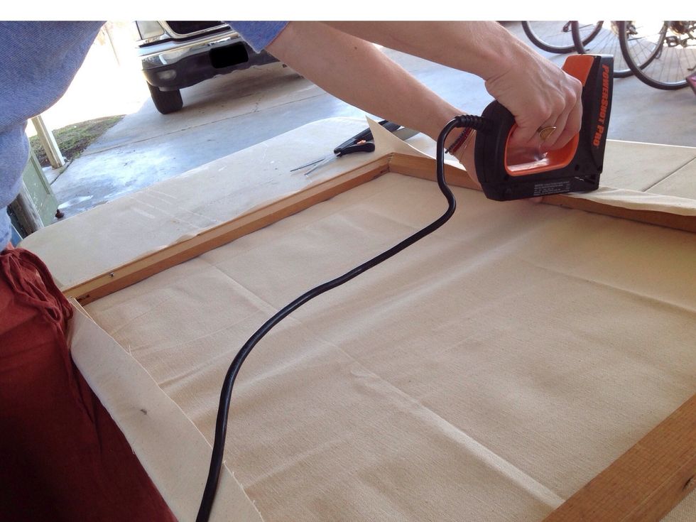 Staple once in the center of one edge. Pull the canvas firmly towards the opposite side and staple in the center there. You do not have to pull too tight, just firm.