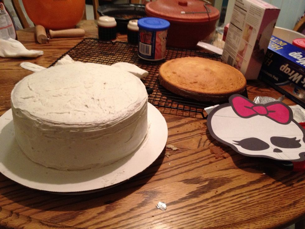 Start by baking the two boxes of cake into four 9-inch round cakes. Level them and layer 3 of them together with frosting. Apply a light layer of frosting on the outside and let it harden.