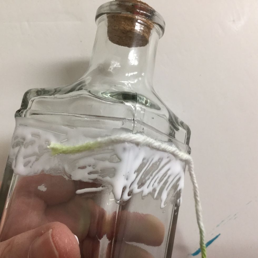 Start winding the yarn around the bottle, gently pressing it into the glue. Allow the end to dip down a bit so it can be covered as you wrap.