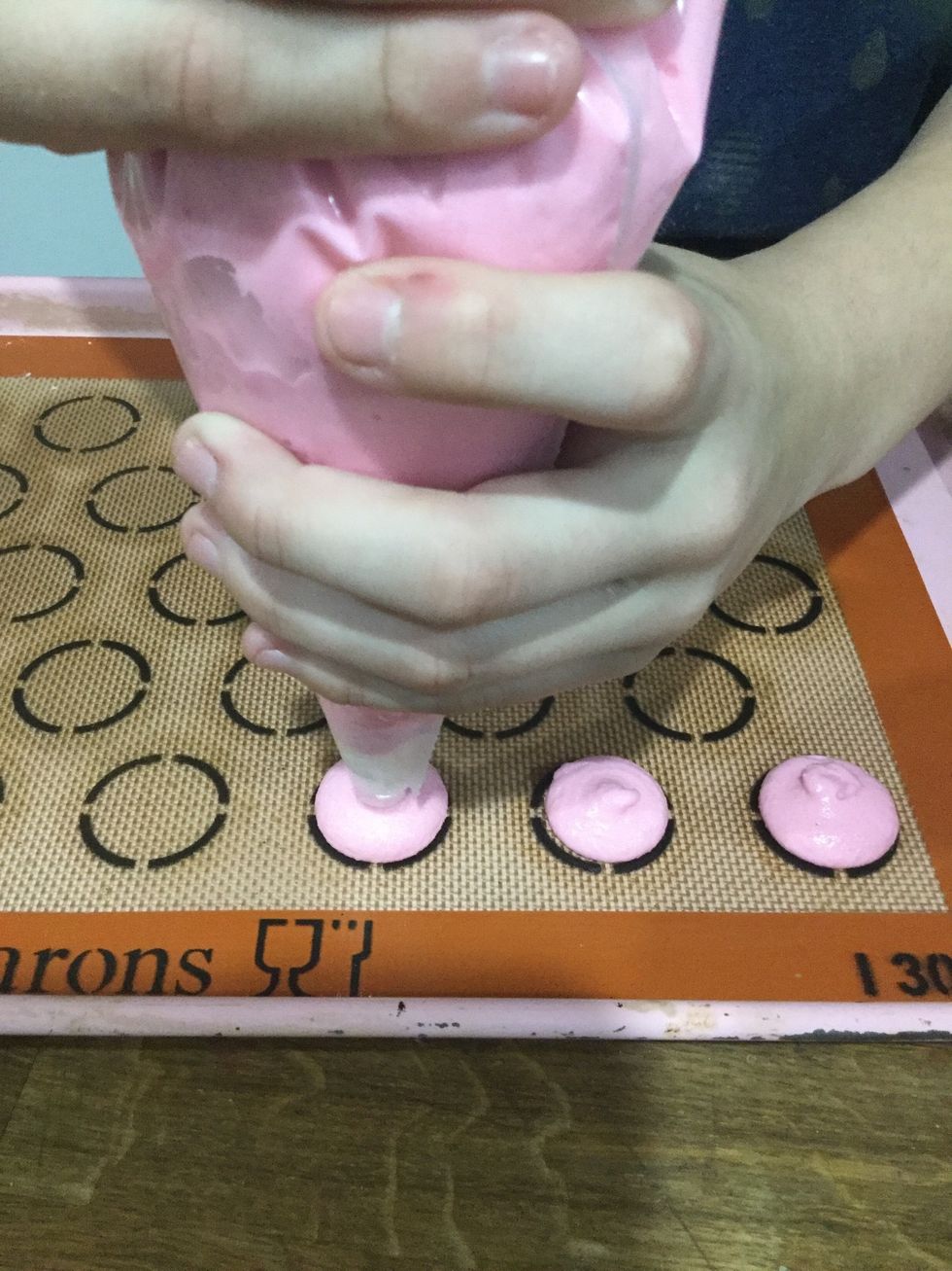 Step 23: Pipe the batter onto silicone mats. When piping, hold the piping tip at a 90 degree angle about 1/4 of an inch above the mat and squeeze gently until the batter almost fills the circle.