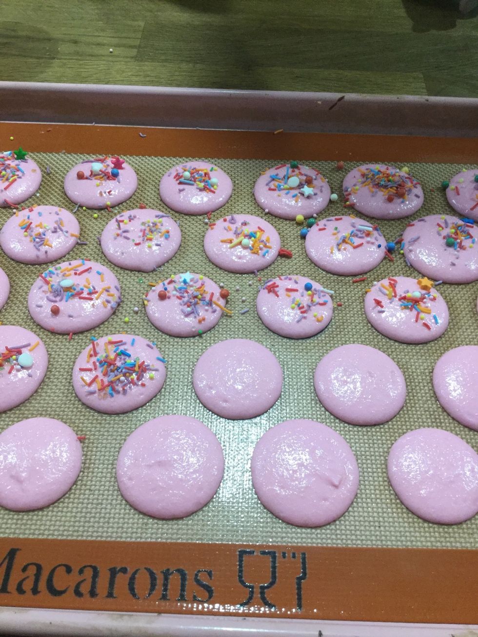 Step 26: After you have banged the batter on the ground so the a smooth and round get a pinch of colourful sprinkles and carefully sprinkle them on the macaron shells.