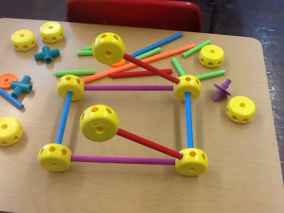 Step 3: Begin to assemble the support for the launcher by putting two red sticks into the top right corner of any two yellow wheels and adding two more yellow wheels onto the tip of the red sticks.