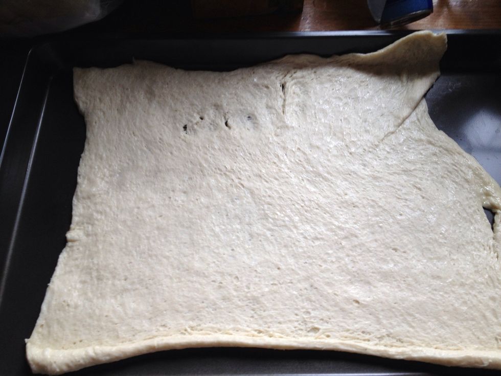 Stretch out pizza dough on a cookie sheet.