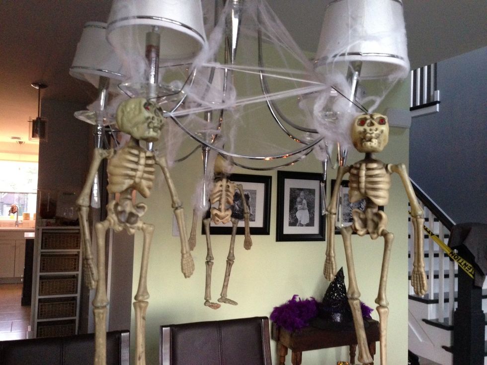 Stretch the white spider web over your lighting fixture in any desired way. Hang the 3 skeletons on the lighting fixture, distributing them evenly.