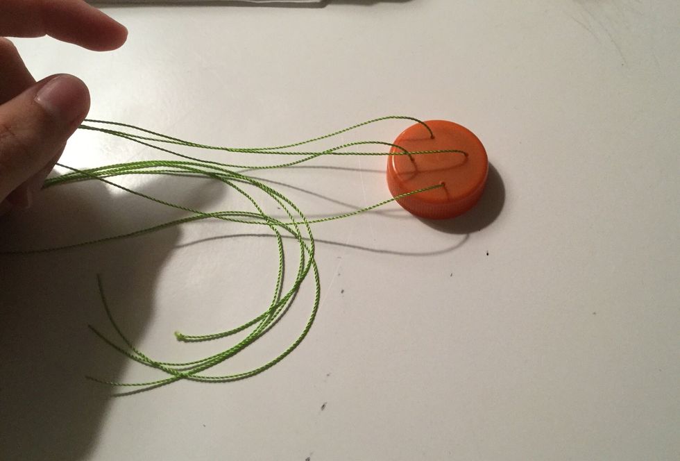 String two long pieces of thread through the four holes so that they cross in the middle, and leave a long strand coming out of each hole.