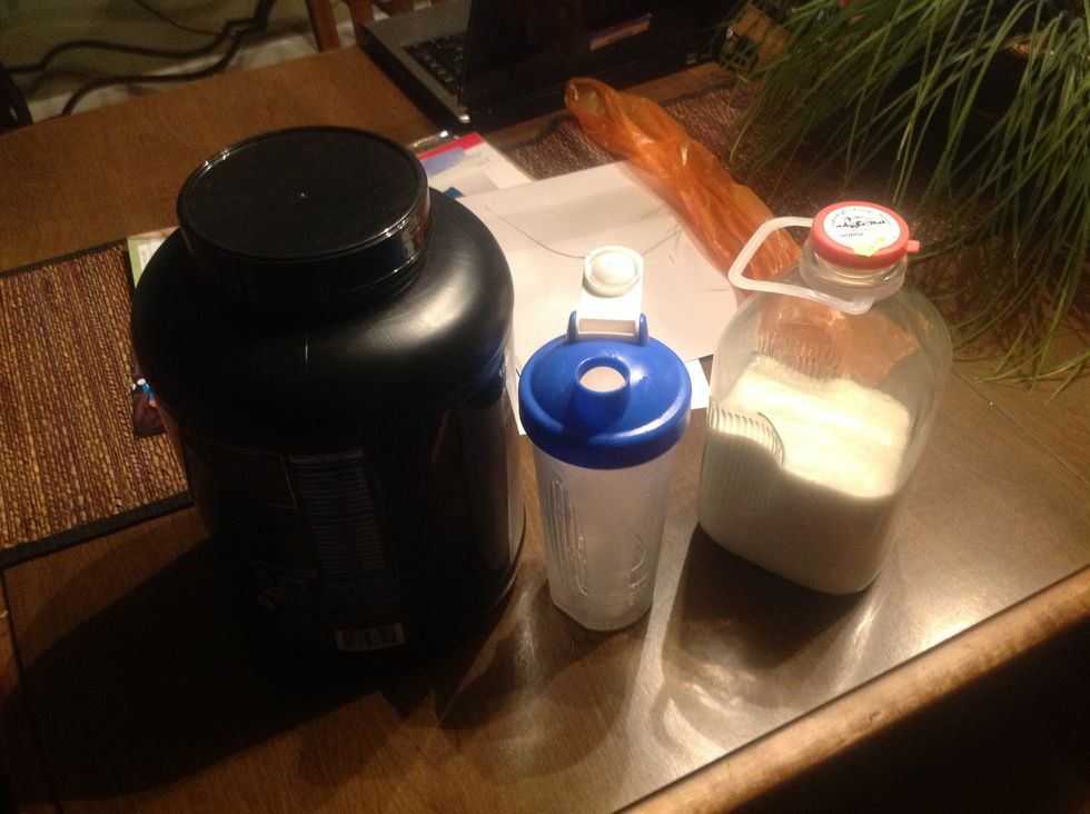 Supplies for making a protein shake. You need protein mix, a cup, and milk.