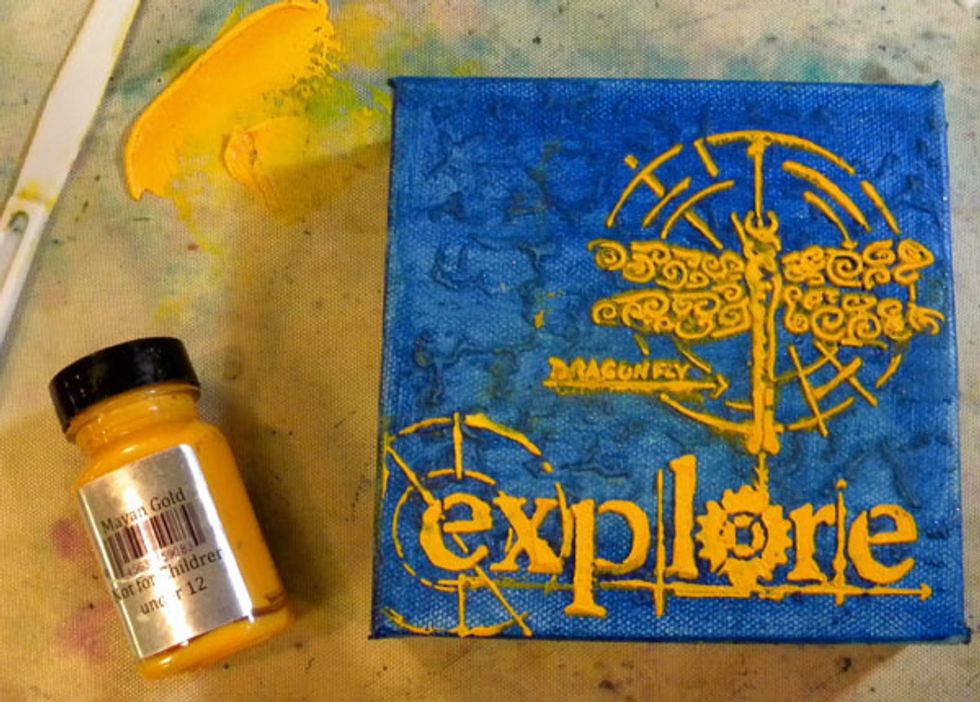 Swipe the mixture through the Explore stencil using a palette knife. Let this layer dry for about an hour.  Use a heat tool if you want to speed up the process.