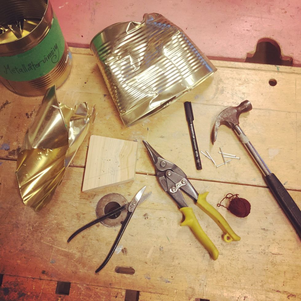 Ta fram en gammal metallburk, metallsax, permanentpenna, spik, hammare, tr\u00e4spillbit och ett garn eller sn\u00f6re.