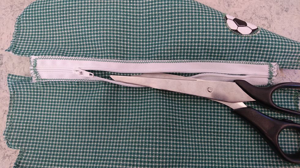 Ta fram en tygsax och klipp bort tyget som \u00e4r under dragkedjan. B\u00f6rja p\u00e5 mitten och..