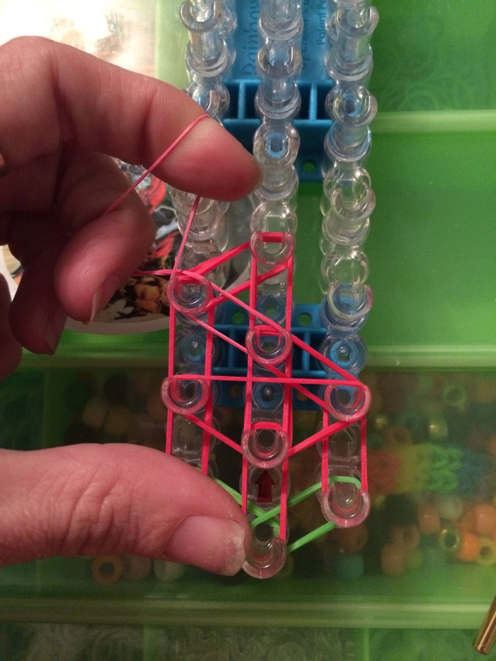 Take 1 red band and double it over the third peg on the center row and the third peg on the left side.