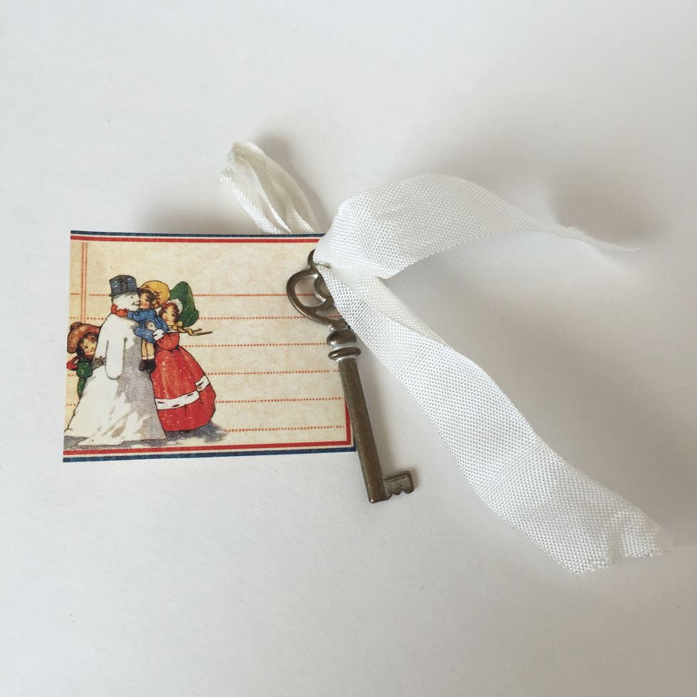Take a 8\u201d or longer length of seam binding and fold in half. Thread the folded end through the top of an Ornate Brass Key and then through the Snowman cutout.