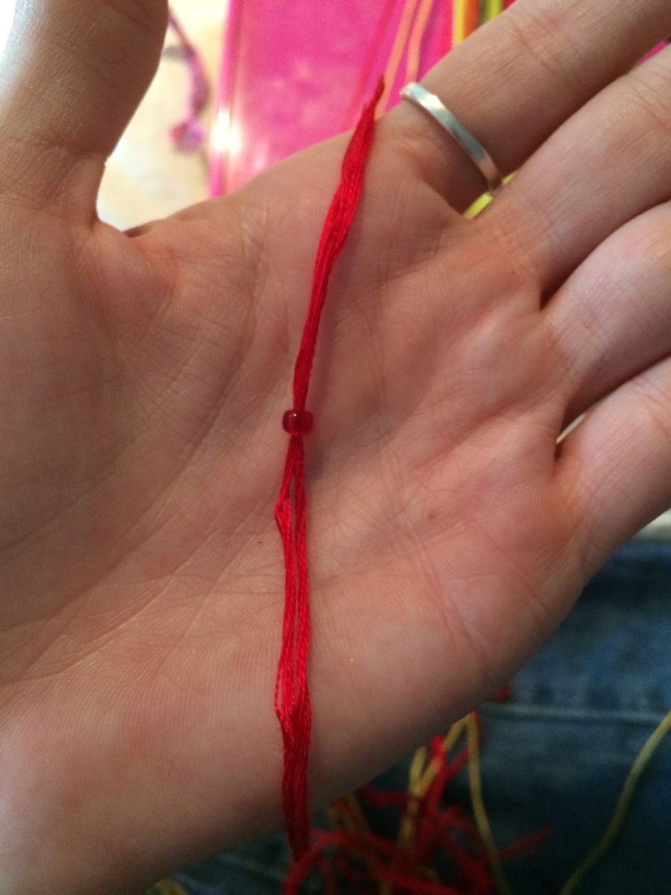 Take a bead and slide the string through the bead. What helps me the most with put using a needle is getting the end if the strings a little wet. This will help slide the bead on a lot easier.