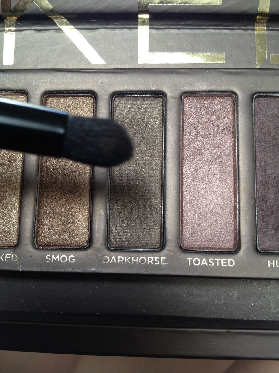 Take a different clean eyeshadow brush and dab a bit of the dark brown shadow such as "Darkhorse". Make sure to use this product sparingly depending on the pigmentation of your eyeshadow.