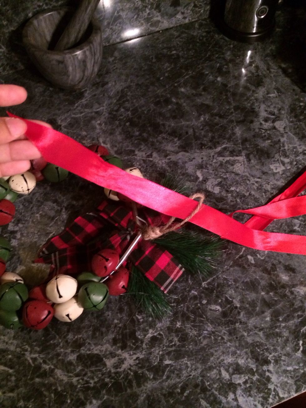 Take a ribbon, any ribbon you want. Some wreaths have a little string in the back,locate it and pass the ribbon through it. If it doesn't just pass the ribbon through the wreath