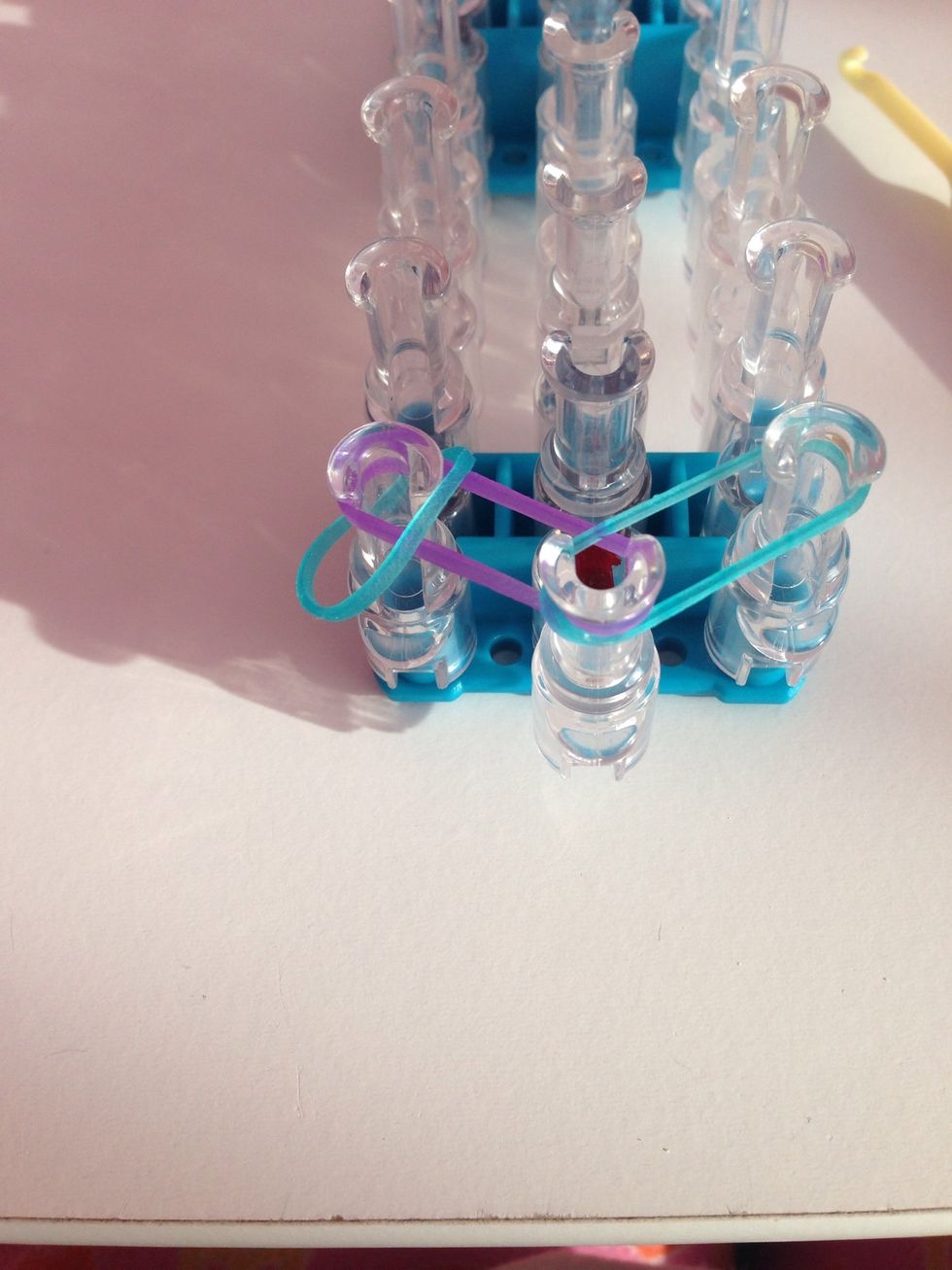 Take a rubber band and place on the left peg on the purple rubber band.