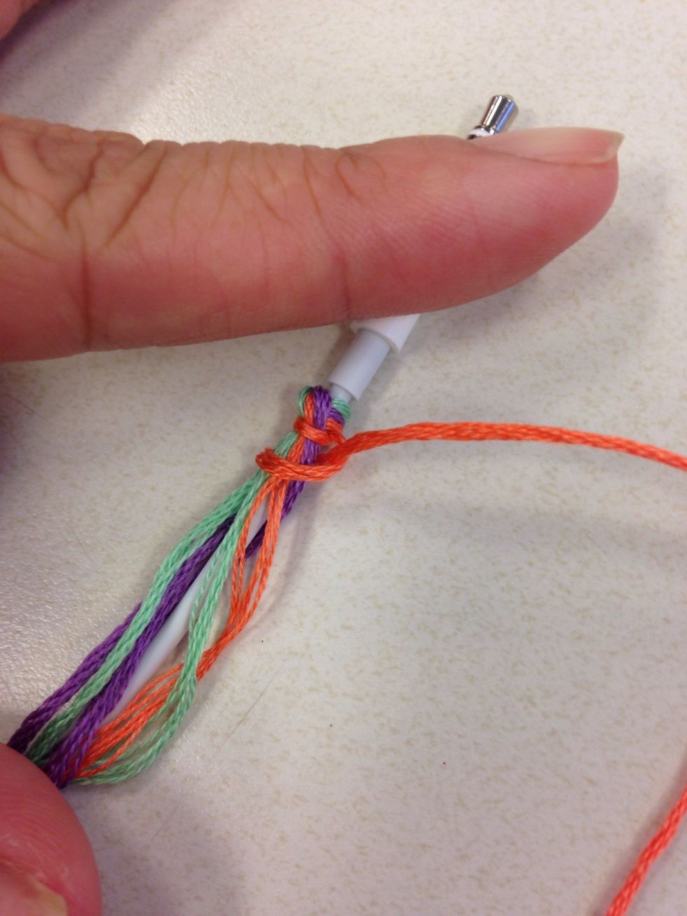 Take one color (peach) long strand separate and grab the rest of the strands against the headphones. Use the peach strand and start making knots.