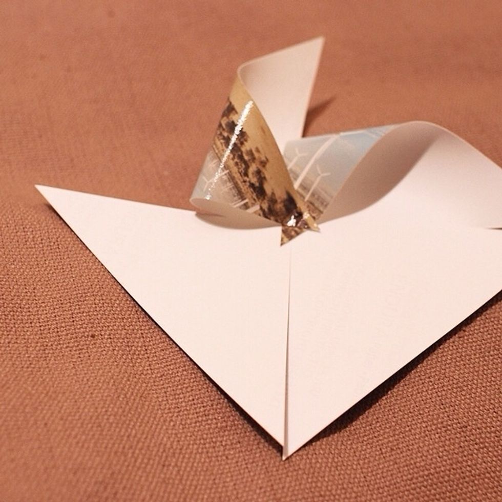 Take one corner and pierce it in the middle with the brad. It\u2019s up to you which corner, but if you use the right side, all 4 have to be the right side. Open up the brad to secure it into place.