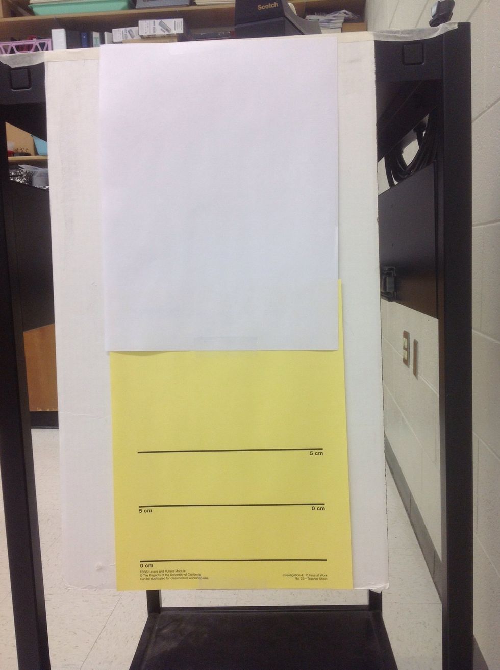 Take one sheet of  white paper and attach it to the top of the cardboard.  Use scotch tape on the top and reinforce it on the bottom by attaching it to the yellow "starting line" paper.