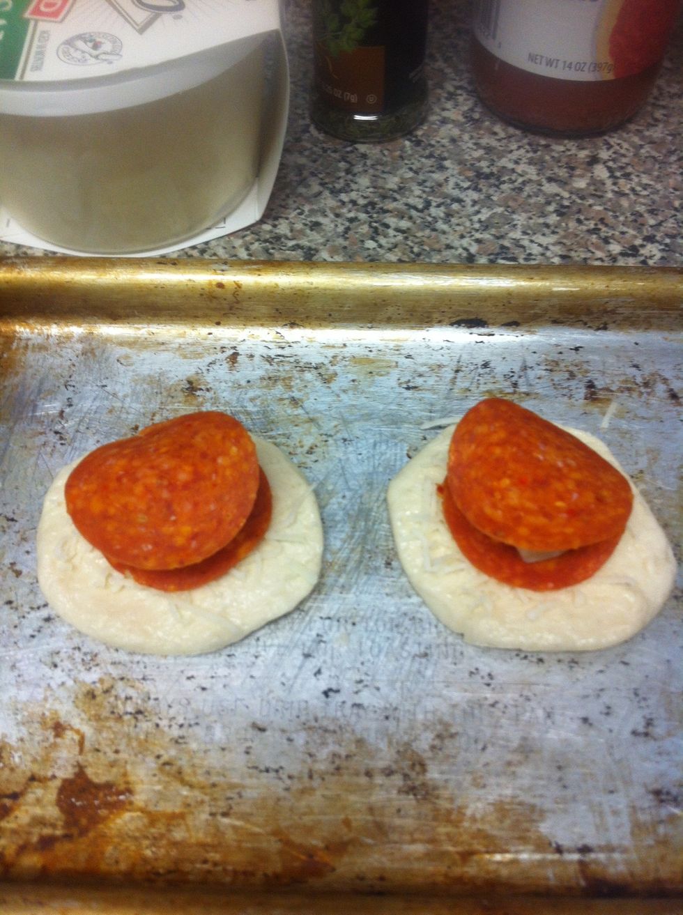 Take pillsbury biscuit dough and flatten, then taking 2 slices of pepperoni and a piece of mozzarella cheese and stack on top of the dough.