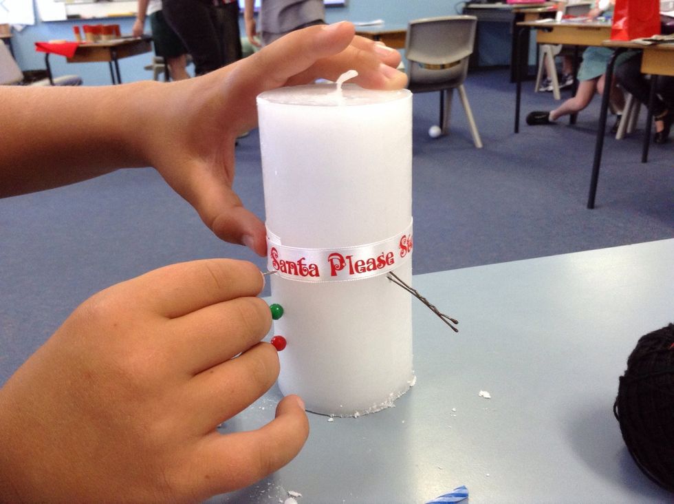 take the 27cm ribbon, then take the top pin out of the candle and then wrap the scarf around the snowman and put the top pin back in