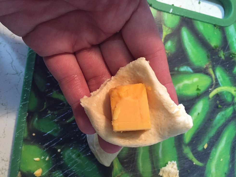 Take the dough and one cube of cheese, wrap and roll it.