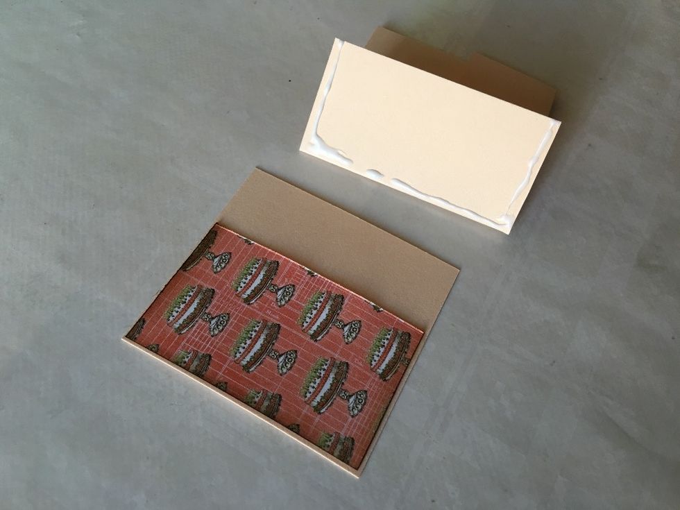 Take the first pocket page piece and fold its left flap closed. Now apply wet glue to both of its sides and along the fold, as shown.