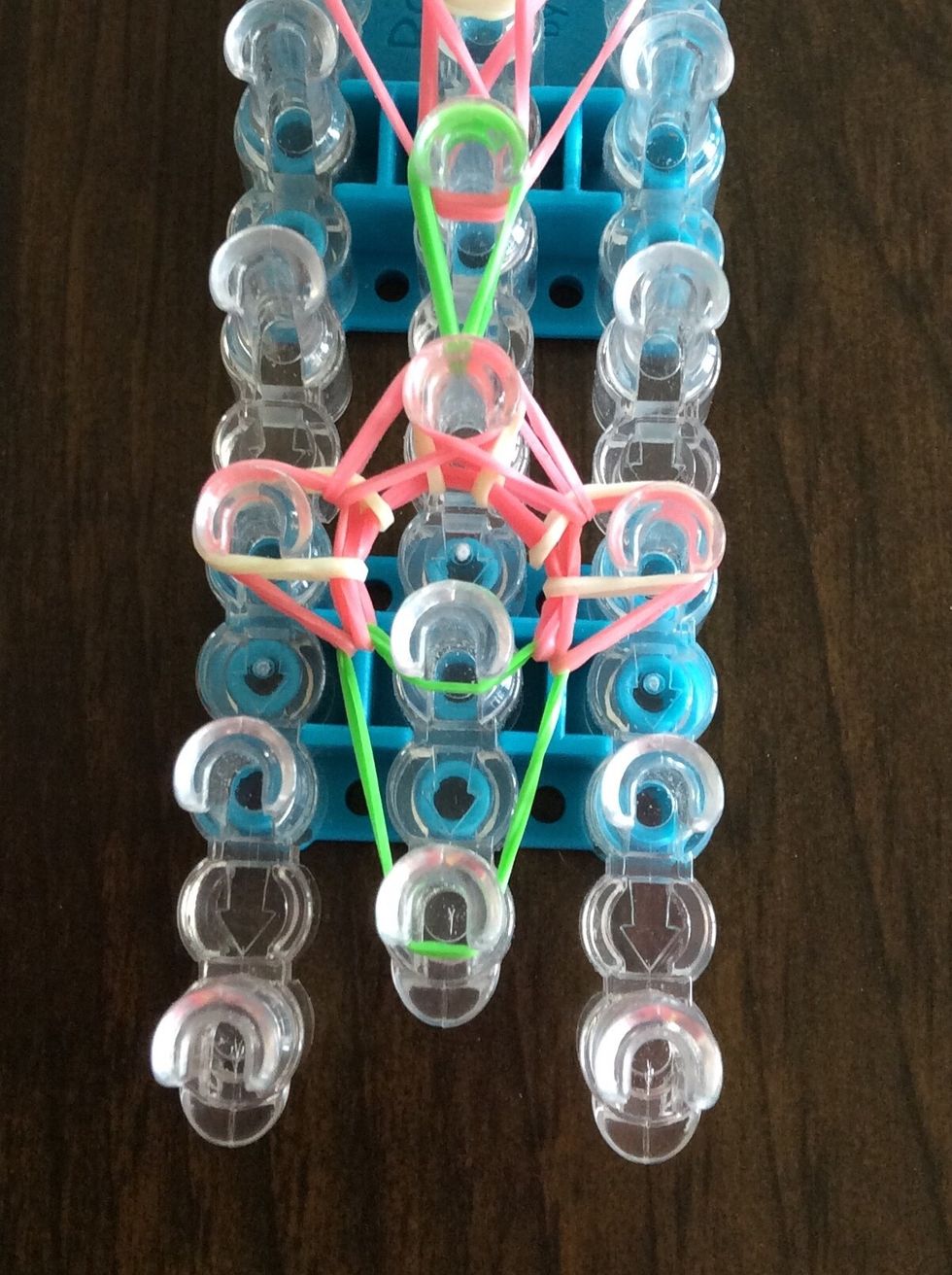 Take the green band on the third middle peg and take it to the fourth middle peg.