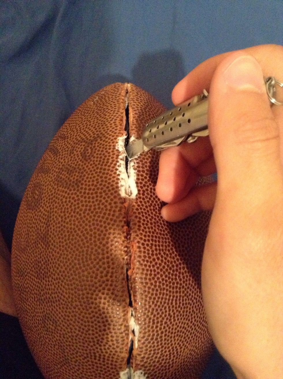 Take the knife and poke it into the lacing on the back of the football..and slowly and carefully cut from one side to the other across the back of the football.