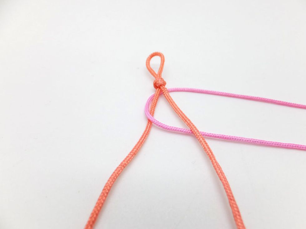 Take the left pink knotting cord and weave it over the left strand of orange cord and then under the right orange cord.