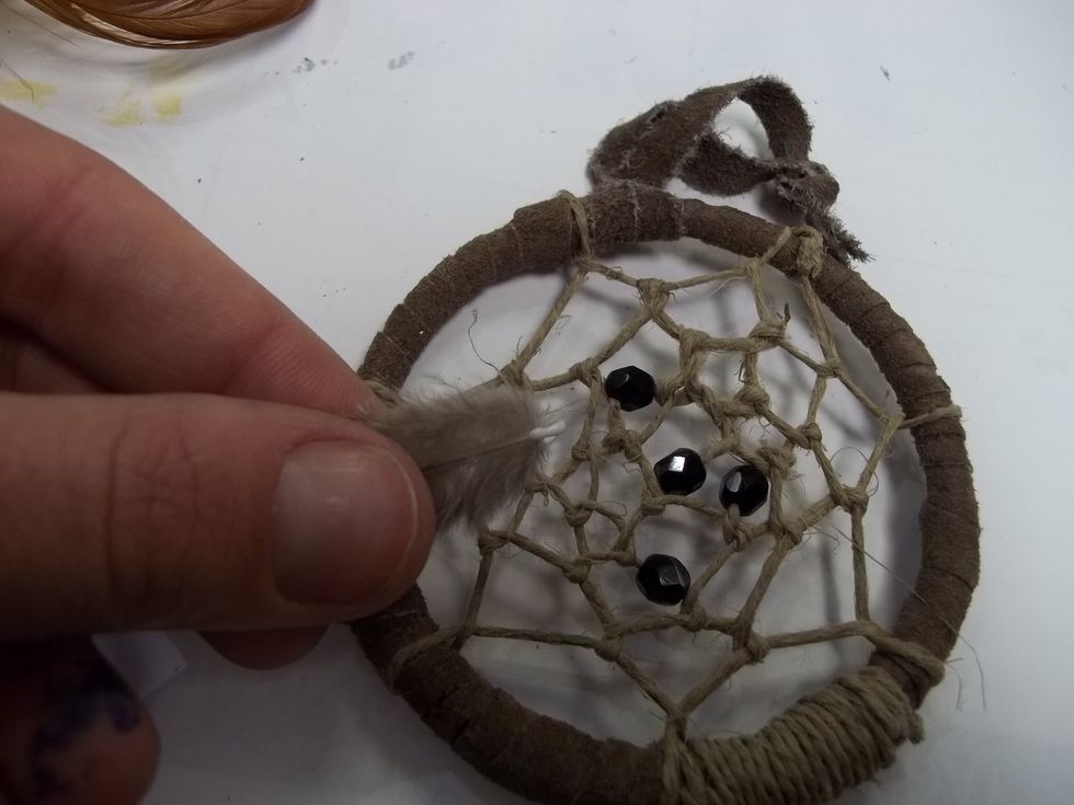 Take the odd ball feather, apply a small amount of glue to it's tip and insert it into one of the knots in the center of your weave.