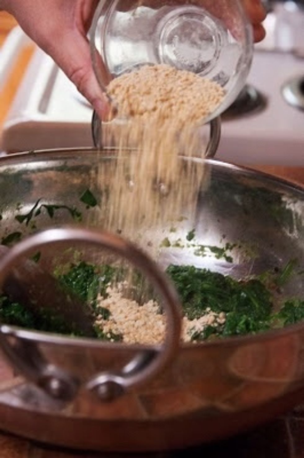 Take the pan off the fire and stir the toasted gram flour into the spinach.