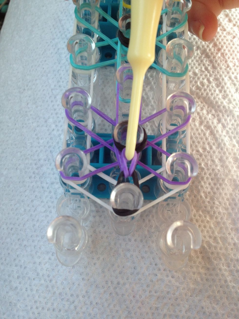 Take the (purple) rubber band from the first peg as pull it over the cap band on to the middle peg.