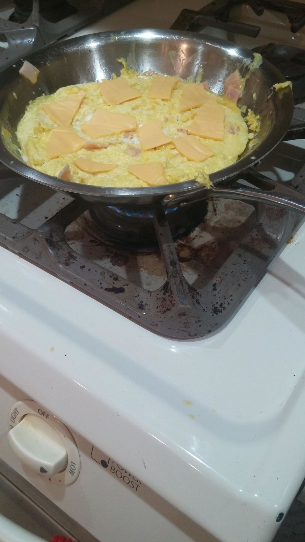 Take the slice of cheese, and either cut it up, or rip it apart. Then spread the pieces evenly on the eggs so they melt on the most surface area.