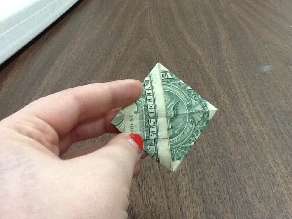 Take the top left corner and fold it in, just like you did with the bottom half. Match the lines you've created, making your dollar now look like a diamond. Or a square. Whichever one you prefer.
