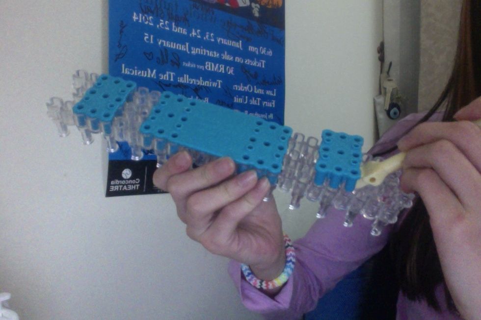 Take you hook and flip your loom around. Use the other side to take the first holder off.